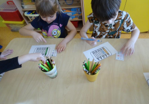Dzieci kolorują kredki zgodnie z instrukcją na kartce.
